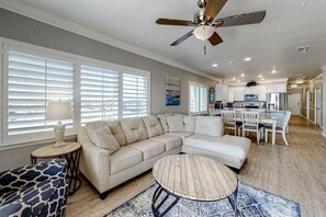 A modern living room with a sectional sofa, a round coffee table, and a dining area with white chairs. - Marlin Key 2A (Orange Beach)
