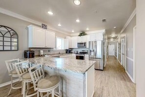 A modern kitchen with white cabinets, a marble island, and stainless steel appliances. - Marlin Key 2A (Orange Beach)