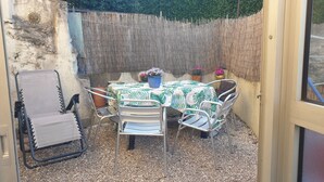 En hyggelig udendørs terrasse med et bord, stole, en flethegn og krukker med planter.