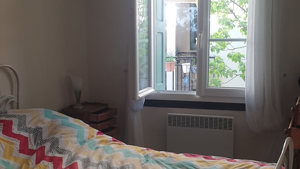 Et soveværelse med seng, et vindue med gardiner, en radiator og et lille bord med lampe.
