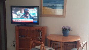 En opholdsstue med fjernsyn, et træskab, et lille bord med en potteplante og et billede i ramme på væggen.