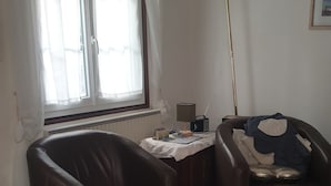 En stue med to læderstole, et lille bord med en radio og et vindue med gardiner.