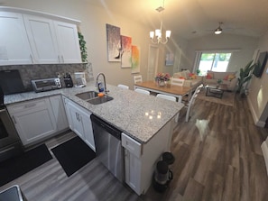 A modern kitchen with granite countertops, white cabinets, a built-in dishwasher, and a coffee maker. - Family Friendly Gem 10 min to Ybor & Downtown! (Tampa)