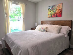 A bedroom with a large bed, a wooden headboard, a colorful painting on the wall, and a window with curtains. - Family Friendly Gem 10 min to Ybor & Downtown! (Tampa)