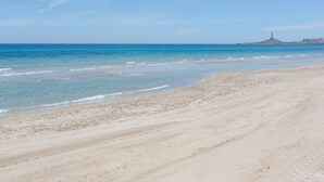 A beach with clear water, a sandy shore, and a distant island with a lighthouse. - Apartment 'Cozy Sea View Flat' with Sea View, Wi-Fi and Air Conditioning (La Manga)