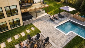 Een modern huis met terras, buitenmeubels, een zwembad en een vuurkorf.
