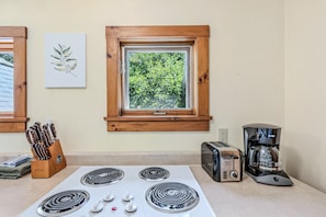 Una cocina con estufa, tostadora, cafetera y ventana con vista a zonas verdes.