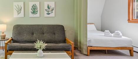 A bedroom with a bed, a sofa, a bedside table, a lamp, and a window.