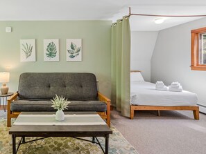 Un dormitorio con cama, sofá, mesita de noche, lámpara y ventana.