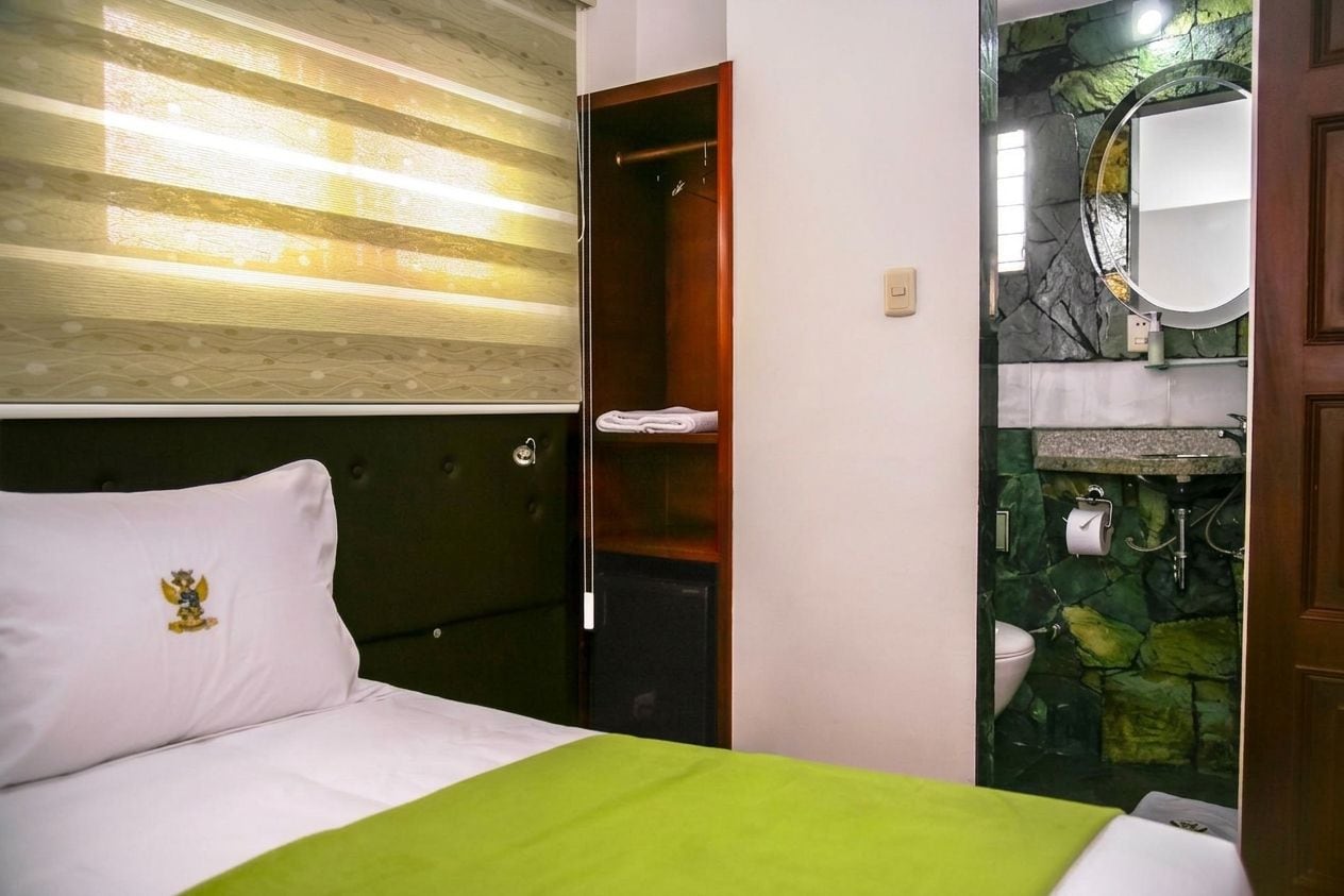 A hotel room with a bed, a closet, and a bathroom with a stone wall and a round mirror.