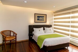 A hotel room with a bed, a chair, a nightstand, a framed picture on the wall, and a window with blinds. - CASA LAVIM  (Bogotá)
