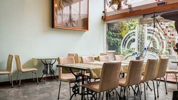 Uma sala de jantar com uma mesa grande e cadeiras, um lustre e vista pela janela.