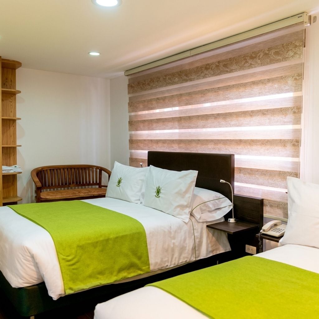 Une chambre d’hôtel avec un lit, une table de chevet avec un téléphone, un banc en bois et un mur orné de rayures horizontales.
