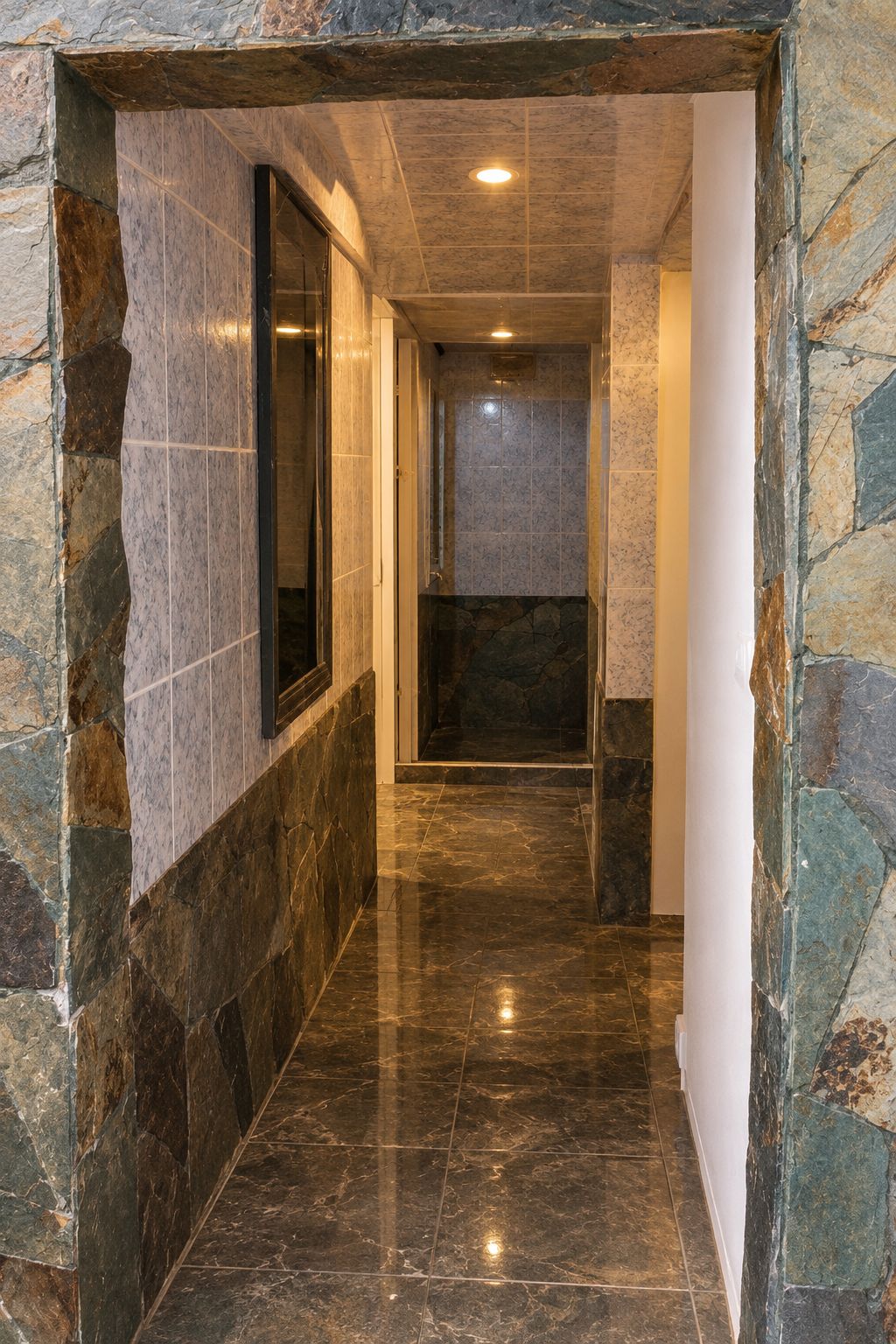 Un pasillo con paredes de piedra y suelo de baldosas, que conduce a una habitación con ventana.
