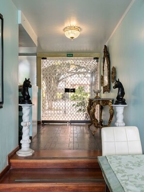 A hallway with a chandelier, a white chair, a table with a horse statue, and a decorative gate. - CASA LAVIM  (Bogotá)