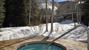 Une terrasse en bois avec un jacuzzi, le tout entouré de neige.