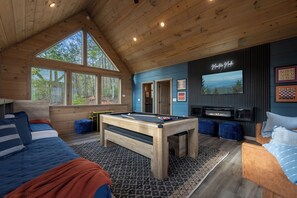 A cozy room with a pool table, a sofa, a TV, and large windows overlooking a forest. - Cabin In The Sky! Fresh Design, Sauna, Unreal View! (Gatlinburg)