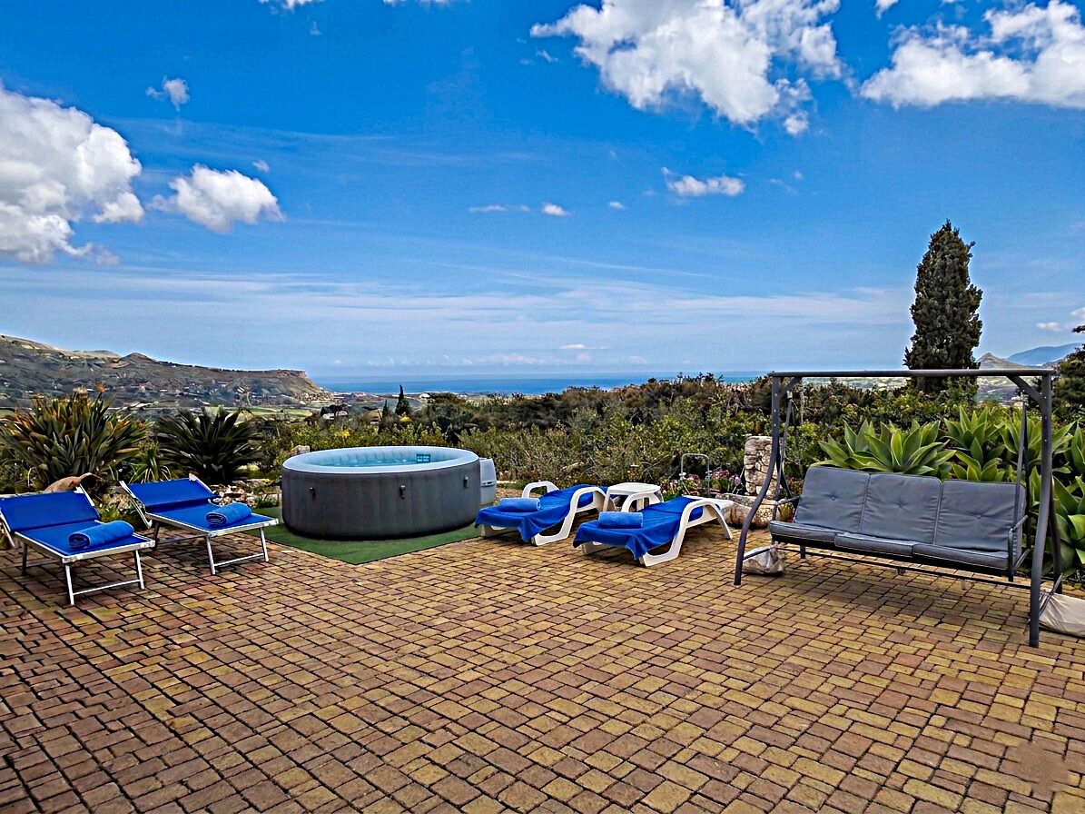 A pool area with lounge chairs, a hot tub, and a view of the landscape.