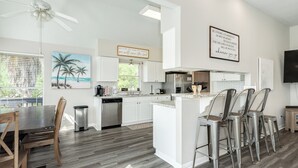 A modern kitchen with white cabinets, a central island with bar stools, a ceiling fan, and a view of the outdoors. - 2 blocks to beach, 13 mi to Downtown - Dog Friendly & Great for Families! (Galveston)