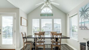 A dining area with a ceiling fan, a sign reading 'BEACH HOUSE,' and a view through large windows. - 2 blocks to beach, 13 mi to Downtown - Dog Friendly & Great for Families! (Galveston)