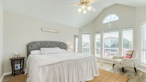 A bedroom with a large bed, a ceiling fan, a window with blinds, and a chair. - 2 blocks to beach, 13 mi to Downtown - Dog Friendly & Great for Families! (Galveston)