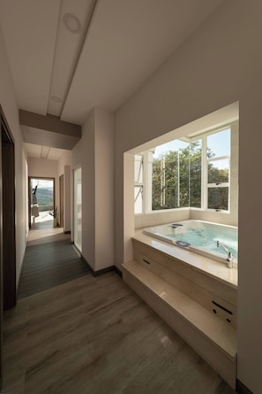 A modern bathroom with a large window, a built-in bathtub, and a wooden floor. - Luxurious 4-bedroom House in Alajuela, Costa Rica (Guacima)