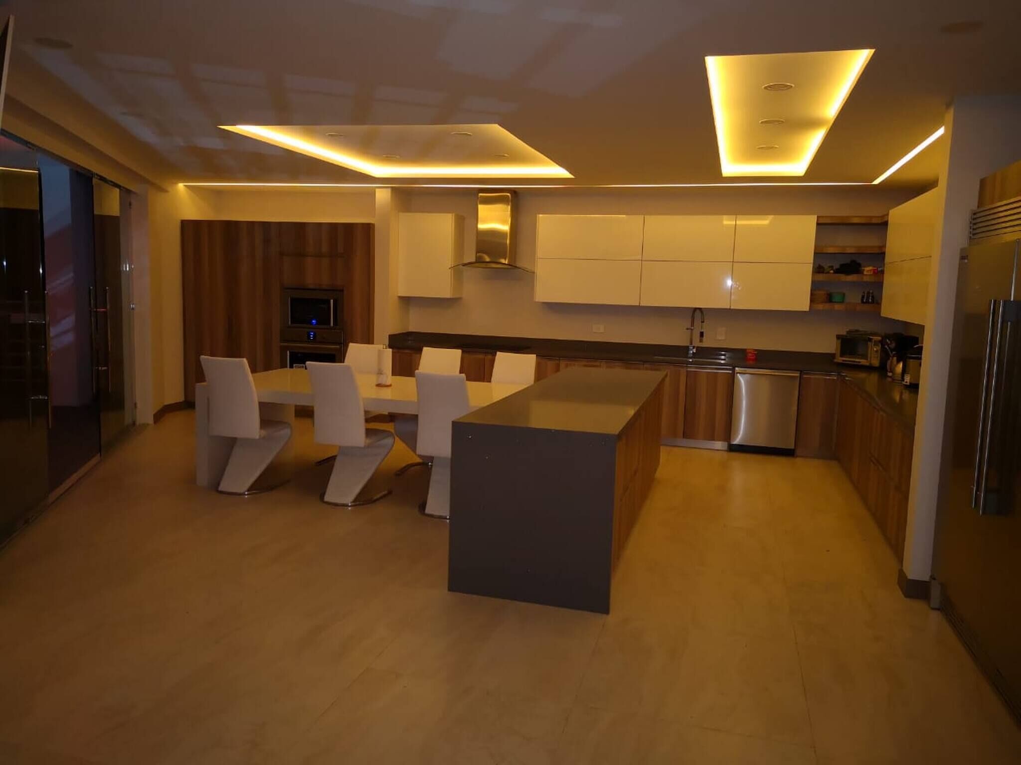 A modern kitchen with a central island, built-in appliances, and a dining area with white chairs.