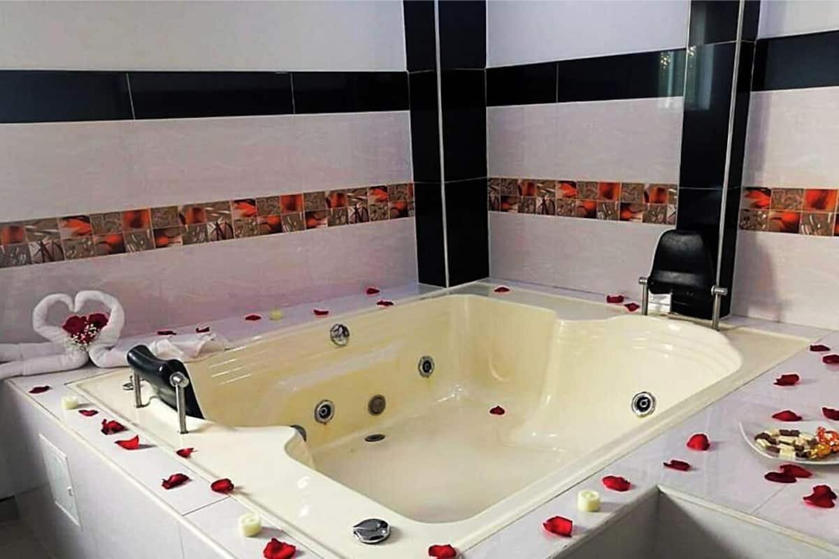Una bañera grande con pétalos de rosa, una silla negra y una toalla sobre una encimera blanca.