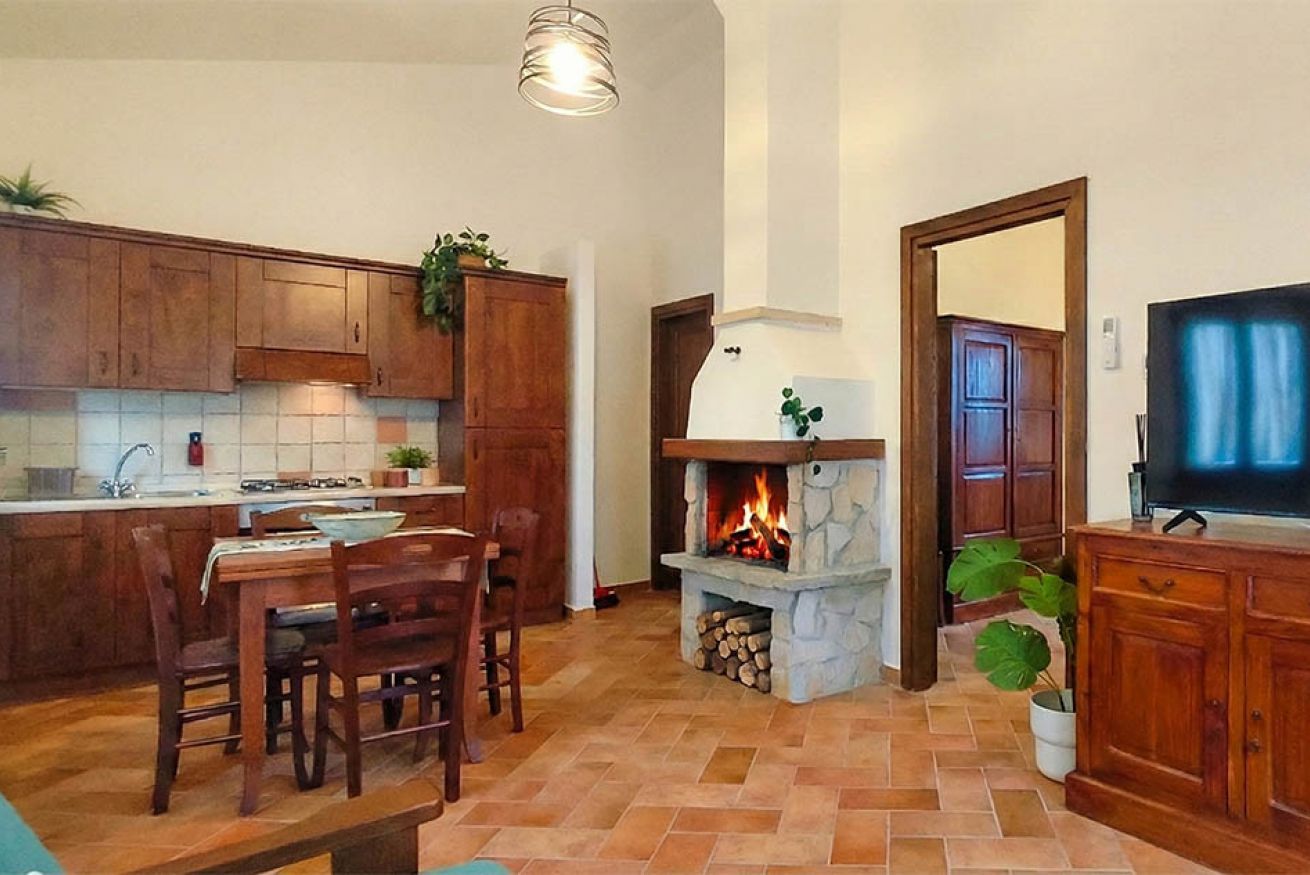 A kitchen with wooden cabinets, a dining table with chairs, a fireplace, and a television on a wooden cabinet.