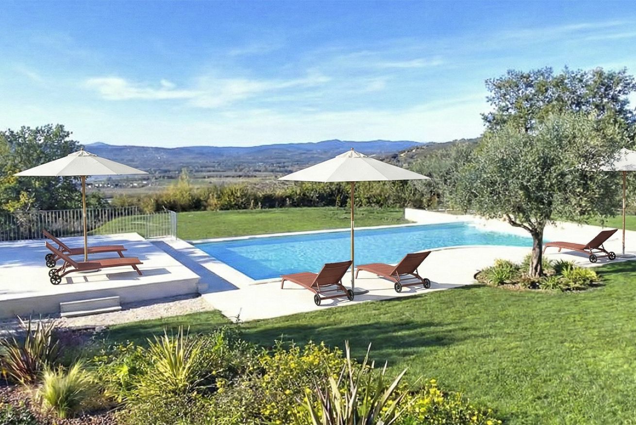 Une piscine entourée de chaises longues et de parasols, elle-même bordée d’une pelouse bien entretenue et d’arbres.