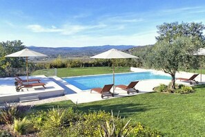 A swimming pool with lounge chairs and umbrellas, surrounded by a well-maintained lawn and trees.