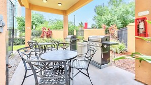 An outdoor patio with a round table and chairs, a grill, and a red utility box.