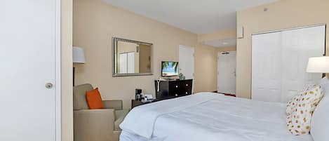 Una habitación de hotel con cama, escritorio, silla, televisor y armario.