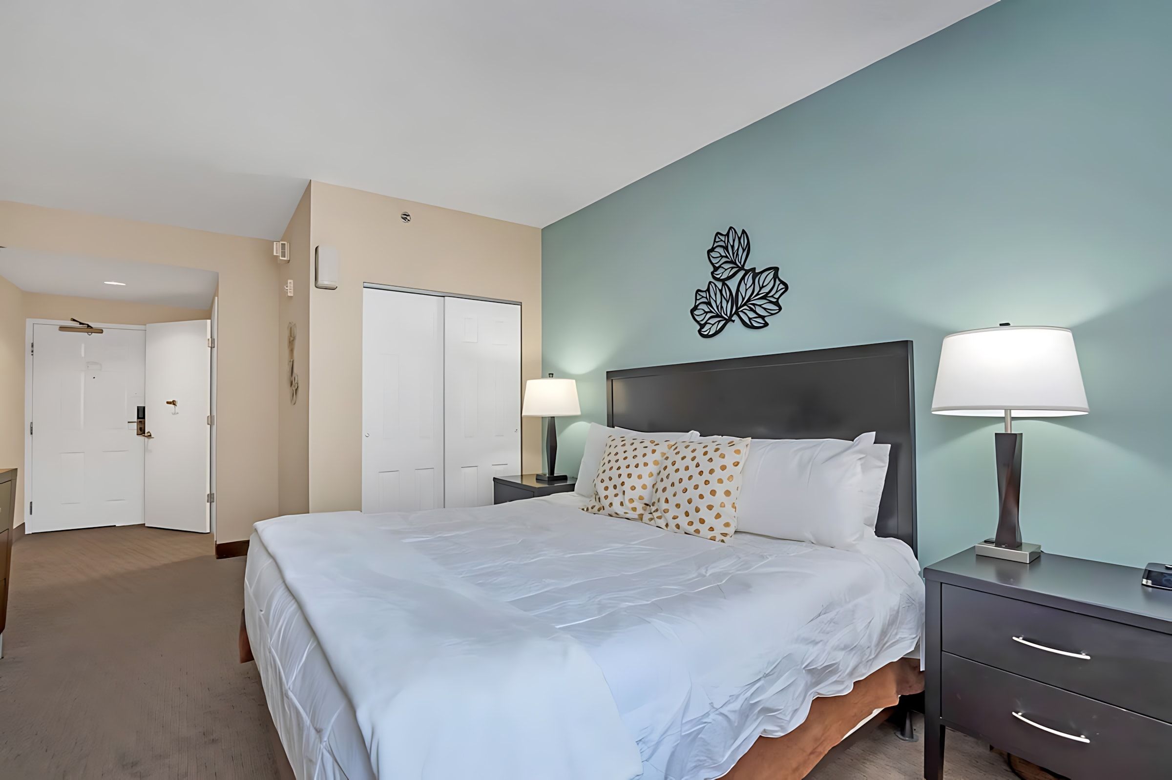 A hotel room with a bed, nightstands, a wall-mounted TV, and a door leading to another room.