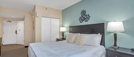 A hotel room with a bed, nightstands, a wall-mounted TV, and a door leading to another room.