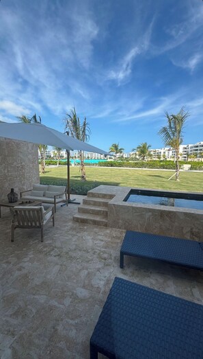 A poolside area with a stone floor, a sofa, a bench, and a view of a pool and buildings in the distance. - Luxury 2-bedroom 2-bathroom condo with jacuzzi and huge pool in  Punta Cana (Punta Cana)
