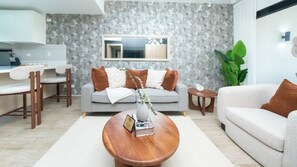 Una sala de estar moderna con un sofá gris, una mesa de centro de madera, y un comedor con sillas y una mesa.