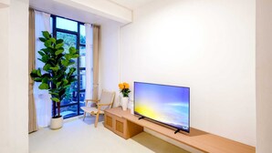 Una sala de estar moderna con un ventanal grande, un televisor de pantalla plana, un banco de madera, una planta en maceta y un jarrón con flores.