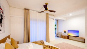 Habitación de hotel con cama, cortinas, ventilador de techo, televisor y vistas al exterior.