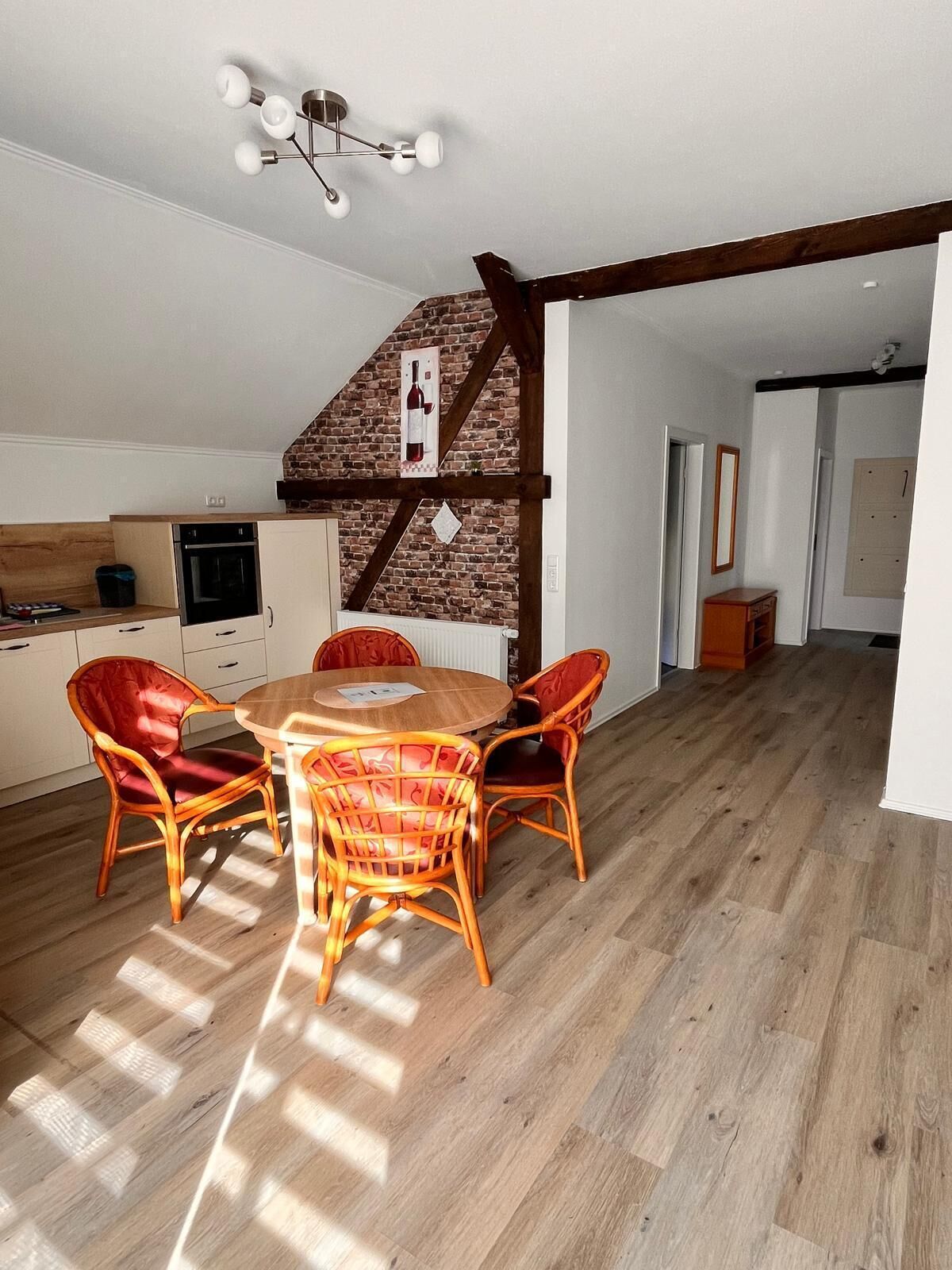 A dining area with a wooden table and wicker chairs, a kitchen with a brick wall, and a ceiling light fixture.