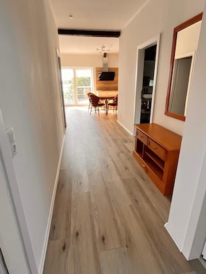 Ein modernes Interieur mit Holzboden, einem Essbereich mit Stühlen, einem an der Wand befestigten Fernseher und einem Holzschrank.