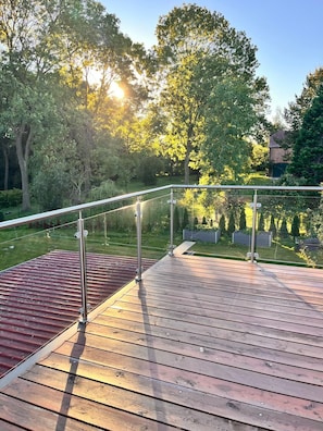 Eine Holzterrasse mit Metallgeländern, umgeben von Bäumen und einer Rasenfläche.