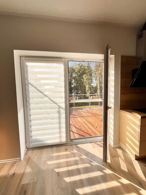 Ein Zimmer mit einer Schiebetür zu einem Außenbereich mit Holzterrasse und Metallgeländer.