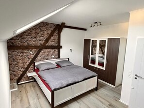Ein Schlafzimmer mit schrägem Dach, einer Wand aus freigelegtem Mauerwerk und einem Kleiderschrank mit Spiegelüren.