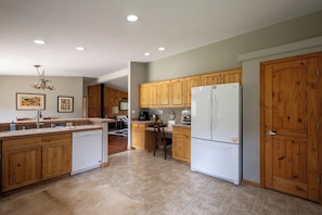 A kitchen with wooden cabinets, a white refrigerator, and a dining area with a chair and table. - Forest Getaway with Jacuzzi! 3 Bedroom Home (Pagosa Springs)