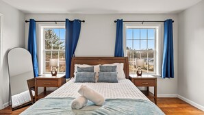 A neatly made bed with pillows, a bedside table with a lamp, and a window with curtains.