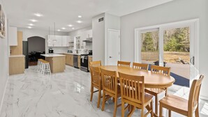 A modern kitchen with white cabinets, a central island, and a dining area with wooden chairs.