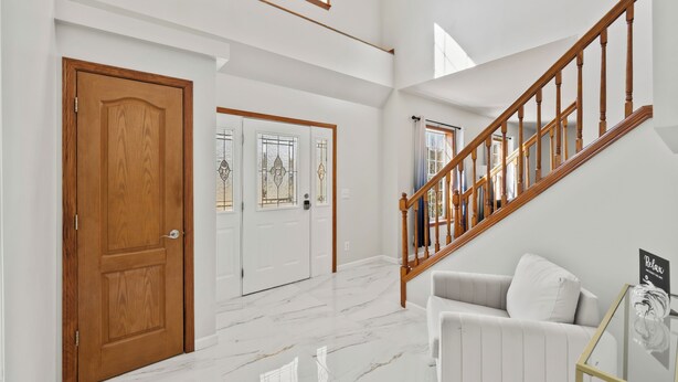 A spacious hallway with a wooden door, a white wall, a staircase with wooden railings, and a white sofa.
