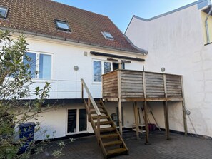 Une maison à deux étages avec une terrasse en bois, un escalier et une fenêtre.