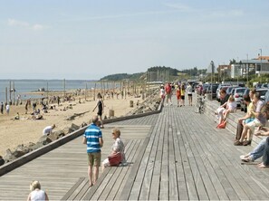 Una passerella di legno che conduce a una spiaggia sabbiosa, con persone che passeggiano e si siedono.